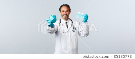 Covid-19, preventing virus, healthcare workers and vaccination concept. Smiling charismatic doctor in gloves and white coat recommend medical respirator and masks, keep social distancing 85180778