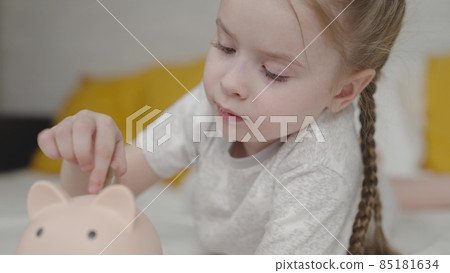 happy little girl throws coins into piggy bank, kid learns count his finances, an interesting baby game, child saves up for dream life, love money from childhood, to be able to save up for purchases 85181634