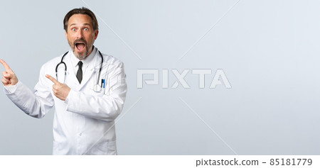 Covid-19, coronavirus outbreak, healthcare workers and pandemic concept. Excited and amazed gasping male doctor, drop jaw and staring camera as pointing upper left corner at banner 85181779