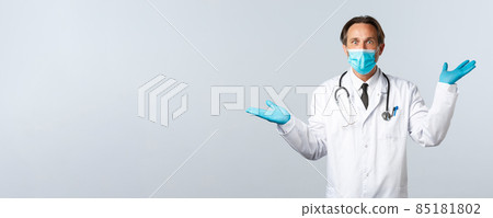 Covid-19, preventing virus, healthcare workers and vaccination concept. Shocked impressed male doctor in medical mask and gloves, raising hands up, showing two products left and right 85181802