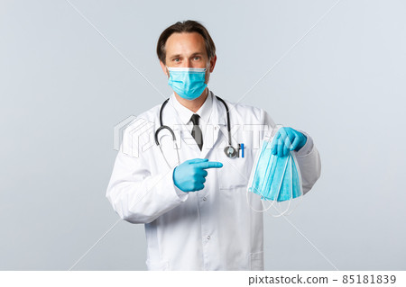 Covid-19, preventing virus, healthcare workers and vaccination concept. Helpful male doctor in PPE pointing at medical masks, recommend using measures to prevent catching coronavirus 85181839