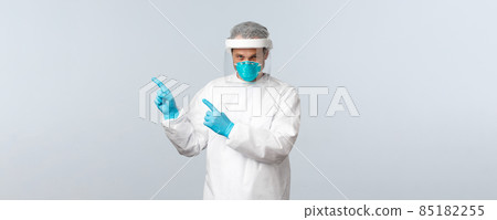 Covid-19, preventing virus, healthcare workers and vaccination concept. Serious doctor in personal protective equipment pointing fingers upper left corner at information banner 85182255