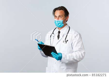 Covid-19, preventing virus, healthcare workers and vaccination concept. Professional doctor in medical mask and gloves, holding clipboard, writing down patient symptoms, fight coronavirus in clinic Covid-19, preventing virus, healthcare workers and vaccination concept. Professional doctor in medical mask and gloves, holding clipboard, writing down patient symptoms, fight coronavirus in clinic 85182271