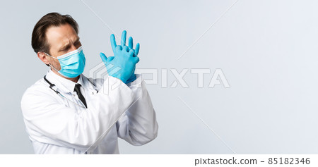 Covid-19, preventing virus, healthcare workers and vaccination concept. Tired doctor in medical mask and gloves squeez hands together, feeling pain in hands after working extra-shifts 85182346