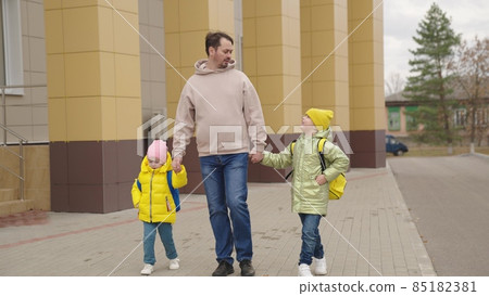school classes, father leads little children with backpacks holding hands, happy family, dad walks with kid around school yard, accompany lessons study, preschool education baby, school bag shoulders school classes, father leads little children with backpacks holding hands, happy family, dad walks with kid around school yard, accompany lessons study, preschool education baby, school bag shoulders 85182381