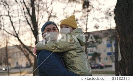 face close-up in mask, little girl in arms of her dad in medical mask smiles in rays sunny city, child with her dad at sunset, to protect herself from coronavirus pandemic, covid 19, code is laughing 85182383