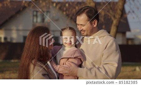 little girl daughter sitting in her mother's arms, happy family, laughing people, father mom and child portrait on the background of the house, moving to a new house of a young couple with a kid little girl daughter sitting in her mother's arms, happy family, laughing people, father mom and child portrait on the background of the house, moving to a new house of a young couple with a kid 85182385