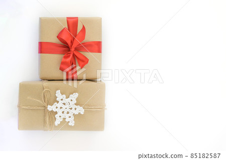 Christmas and New Years flatlay background. Gift box wrapped in kraft paper with jute cord. Decorated with a crocheted snowflake. Box with a red ribbon. Place for your text Christmas and New Years flatlay background. Gift box wrapped in kraft paper with jute cord. Decorated with a crocheted snowflake. Box with a red ribbon. Place for your text 85182587
