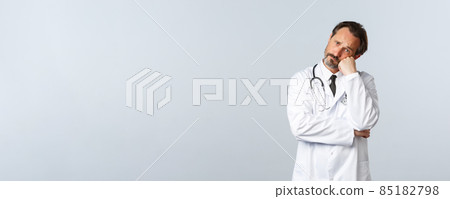 Covid-19, coronavirus outbreak, healthcare workers and pandemic concept. Distressed and sad uneasy male doctor in white coat, lean on hand and look troubled, having problem 85182798