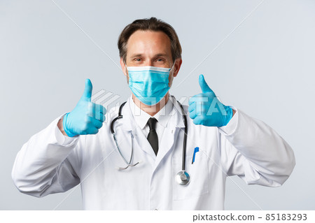 Covid-19, preventing virus, healthcare workers and vaccination concept. Close-up of satisfied middle-aged doctor in medical mask and gloves, show thumbs-up in approval, like and recommend product 85183293