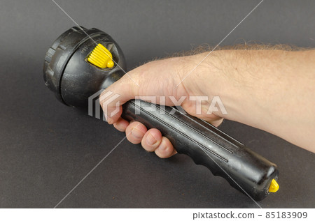A man is holding a large black hand flashlight in his hand. A man is holding a large black hand flashlight in his hand. 85183909