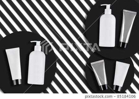 White, gray tubes and pump bottles with no logo or label on black round stands, striped background. Cosmetics packs, containers. Close up, copy space White, gray tubes and pump bottles with no logo or label on black round stands, striped background. Cosmetics packs, containers. Close up, copy space 85184106