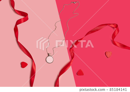 Blank pendant or medallion on a chain next to red ribbons and cut out cardboard hearts against colorful studio background. Close up, copy space 85184141