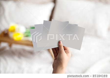 Hand of unknown person holding some empty pieces of paper against blurred bed with white linen and breakfast serving tray on it. Close up, copy space Hand of unknown person holding some empty pieces of paper against blurred bed with white linen and breakfast serving tray on it. Close up, copy space 85184169