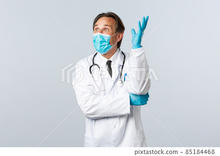 Covid-19, preventing virus, healthcare workers and vaccination concept. Excited upbeat male doctor in medical mask and gloves, raising hand up thoughtful, have idea, look amazed 85184468