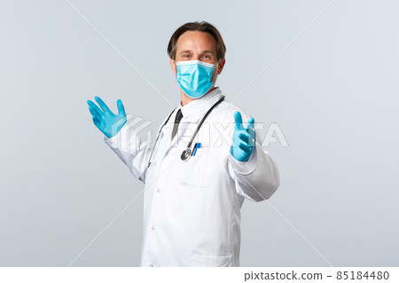 Covid-19, preventing virus, healthcare workers and vaccination concept. Cheerful glad doctor in medical mask and gloves, spread hands sideways relieved, celebrating good news, white background Covid-19, preventing virus, healthcare workers and vaccination concept. Cheerful glad doctor in medical mask and gloves, spread hands sideways relieved, celebrating good news, white background 85184480