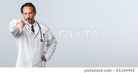 Covid-19, coronavirus outbreak, healthcare workers and pandemic concept. Disappointed serious male doctor in white coat, frowning displeased and show thumb-down, disapprove action 85184493