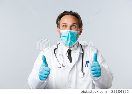 Covid-19, preventing virus, healthcare workers and vaccination concept. Excited and surprised happy doctor in medical mask and gloves, showing thumbs-up thrilled, hear great news, agree and approve 85184525