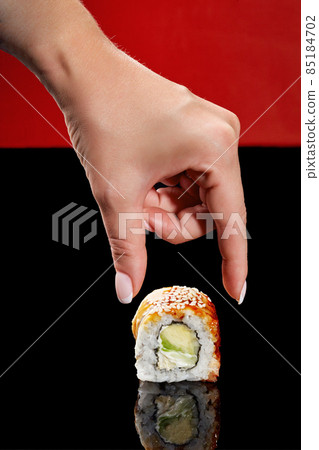 Female hand reaching out to unagi roll with eel, cream cheese and avocado Female hand reaching out to unagi roll with eel, cream cheese and avocado 85184702