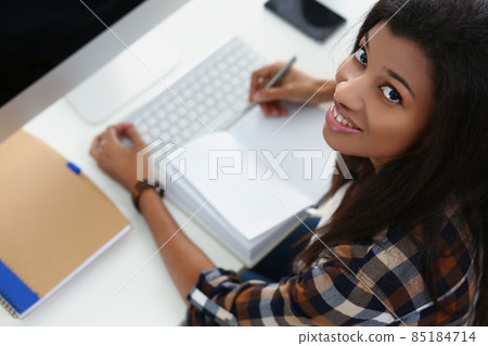 Smiling afro american young woman on workplace, open journal, luxury device on workplace 85184714