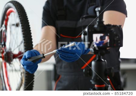 Blogger mechanic fix bicycle in workshop, busy young worker in shirt and gloves Blogger mechanic fix bicycle in workshop, busy young worker in shirt and gloves 85184720