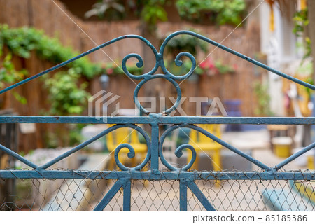 Vintage artistic green wrought iron gate with peeling paint and rust revealing blurred garden 85185386