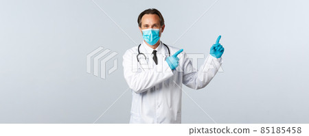 Covid-19, preventing virus, healthcare workers and vaccination concept. Smiling friendly doctor in white coat, medical mask and gloves pointing top right advertisement, white background Covid-19, preventing virus, healthcare workers and vaccination concept. Smiling friendly doctor in white coat, medical mask and gloves pointing top right advertisement, white background 85185458