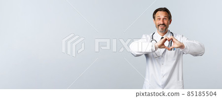 Covid-19, coronavirus outbreak, healthcare workers and pandemic concept. Happy caring male doctor in white coat, showing heart sign and smiling, express sympathy and admiration 85185504