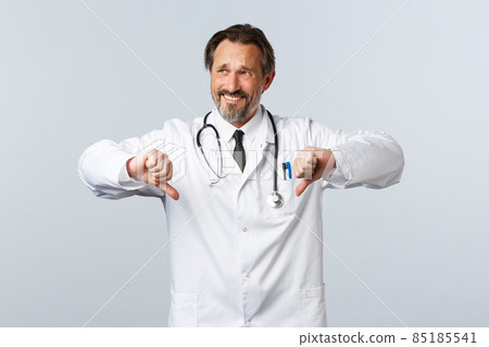 Covid-19, coronavirus outbreak, healthcare workers and pandemic concept. Skeptical and reluctant male doctor in white coat look away grimacing displeased, show thumbs-down 85185541