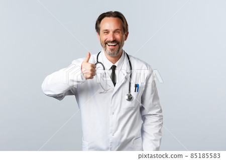 Covid-19, coronavirus outbreak, healthcare workers and pandemic concept. Handsome cheerful male doctor in white coat show thumbs-up in approval, agree or like product, recommending Covid-19, coronavirus outbreak, healthcare workers and pandemic concept. Handsome cheerful male doctor in white coat show thumbs-up in approval, agree or like product, recommending 85185583