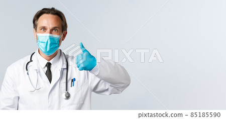 Covid-19, preventing virus, healthcare workers and vaccination concept. Excited happy doctor smiling enthusiastic, wear medical mask and gloves show thumbs-up, agree or approve product 85185590