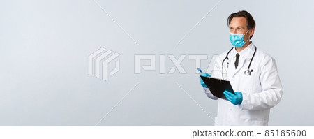 Covid-19, preventing virus, healthcare workers and vaccination concept. Serious professional doctor in medical mask and gloves holding clipboard, look left, examine patient, do tests Covid-19, preventing virus, healthcare workers and vaccination concept. Serious professional doctor in medical mask and gloves holding clipboard, look left, examine patient, do tests 85185600