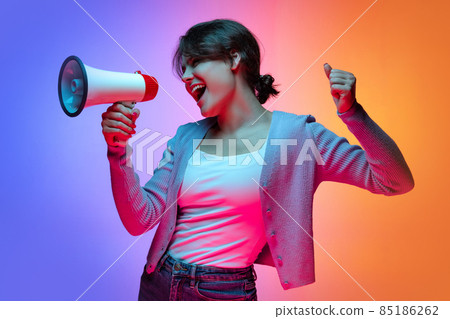 Excited young beautiful girl in warm cardigan shouting at megaphone isolated on gradient blue orange neon background 85186262