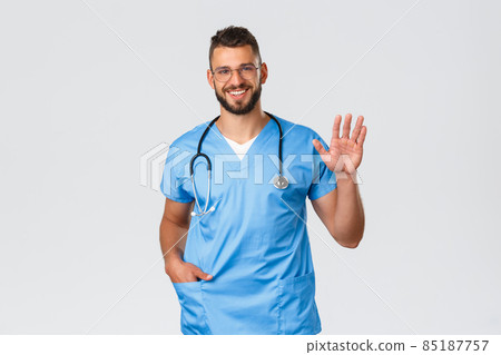 Healthcare workers, medicine, covid-19 and pandemic self-quarantine concept. Friendly doctor, male nurse in scrubs and stethoscope, saying hi to patient or coworker, wave hand in hello Healthcare workers, medicine, covid-19 and pandemic self-quarantine concept. Friendly doctor, male nurse in scrubs and stethoscope, saying hi to patient or coworker, wave hand in hello 85187757