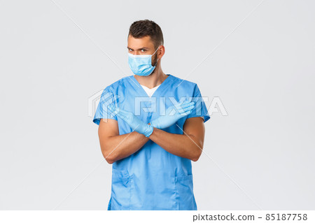 Healthcare workers, covid-19, coronavirus and virus concept. Serious professional doctor, male nurse in blue scrubs and medical mask tell stop, show cross prohibition sign, frowning displeased Healthcare workers, covid-19, coronavirus and virus concept. Serious professional doctor, male nurse in blue scrubs and medical mask tell stop, show cross prohibition sign, frowning displeased 85187758