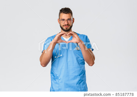 Healthcare workers, medicine, covid-19 and pandemic quarantine concept. Smiling hopeful doctor in blue scrubs, male nurse in scrubs and glasses, make heart sign, care for patients staying safe home Healthcare workers, medicine, covid-19 and pandemic quarantine concept. Smiling hopeful doctor in blue scrubs, male nurse in scrubs and glasses, make heart sign, care for patients staying safe home 85187778