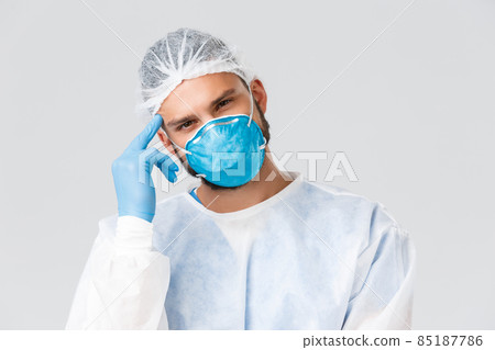 Covid-19 pandemic, virus outbreak, clinic and healthcare workers concept. Young thougtful doctor in personal protective equipment, respirator and gloves, tilt head, thinking serious Covid-19 pandemic, virus outbreak, clinic and healthcare workers concept. Young thougtful doctor in personal protective equipment, respirator and gloves, tilt head, thinking serious 85187786