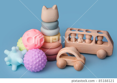 Colorful educational montessori kids toys on a blue background. Sensory balls for kids, wooden cars and silicone pyramid, textured plastic multi ball set for babies and toddlers, tower toy 85188121