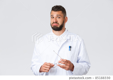 Healthcare workers, coronavirus, covid-19 pandemic and insurance concept. Handsome unsure doctor in medical white coat, hold glasses, pouting indecisive, listen to interesting point view Healthcare workers, coronavirus, covid-19 pandemic and insurance concept. Handsome unsure doctor in medical white coat, hold glasses, pouting indecisive, listen to interesting point view 85188330