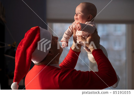 Caucasian grandfather in red hat playing with granddaughter at home selebrating Christmas 85191035