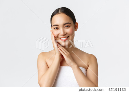 Tender beautiful asian girl in towel standing over white background in bathroom, apply skincare products, cleansing gel for face, touching skin and smiling pleased, white background Tender beautiful asian girl in towel standing over white background in bathroom, apply skincare products, cleansing gel for face, touching skin and smiling pleased, white background 85191183