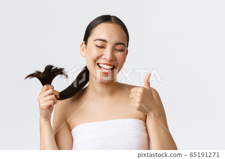 Beauty, hair loss products, shampoo and hair care concept. Close-up of satisfied, happy asian girl in bath towel showing thumbs-up and healthy hair ends, standing pleased white background 85191271