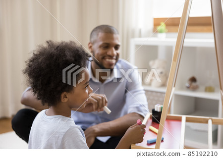 Happy cute Black little kid and dad drawing on chalkboard Happy cute Black little kid and dad drawing on chalkboard 85192210