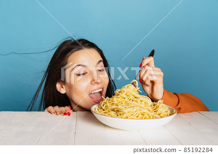 Excited young girl preparing to eat large portion of noodles isolated on blue studio background. World pasta day 85192284