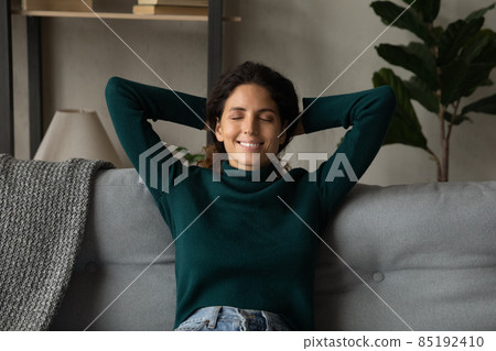 Smiling young latin female rest on couch hands behind head Smiling young latin female rest on couch hands behind head 85192410