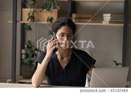 Hispanic woman work on laptop talk on smartphone 85192469