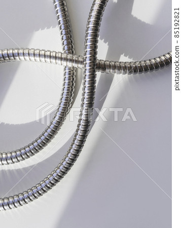 Metal shower hose on white background. Flexible chrome tube. Corrugated plumbing tube on geometrical banner with copy space on hard sunlight and shadow. Metal shower hose on white background. Flexible chrome tube. Corrugated plumbing tube on geometrical banner with copy space on hard sunlight and shadow. 85192821