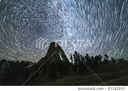Star Trails over Devils Tower Butte at Night. Light Flare of Climbers on a Wall. Wyoming, USA 85192935