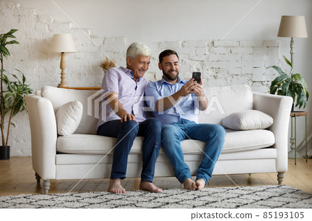 Happy young man using cellphone with older father. Happy young man using cellphone with older father. 85193105