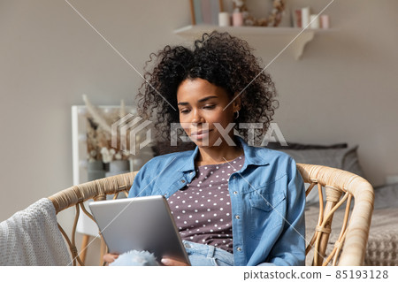 Beautiful African woman sit on cozy wicker armchair with tablet 85193128